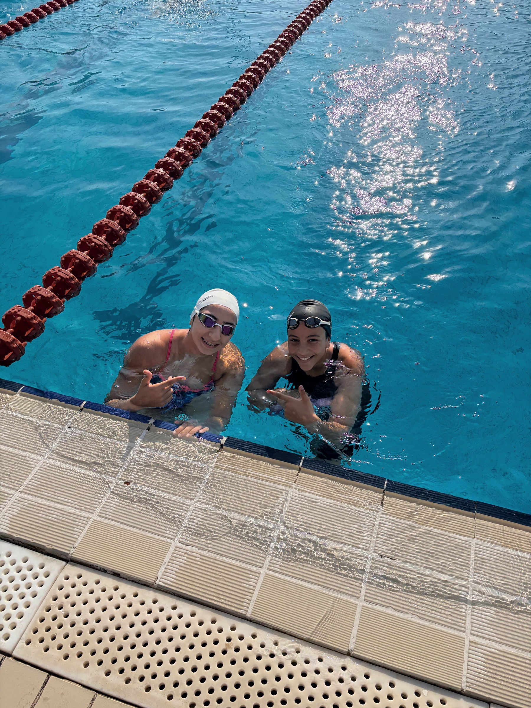 Two SWEEP swimmers smiling up from the wall, sun on the water