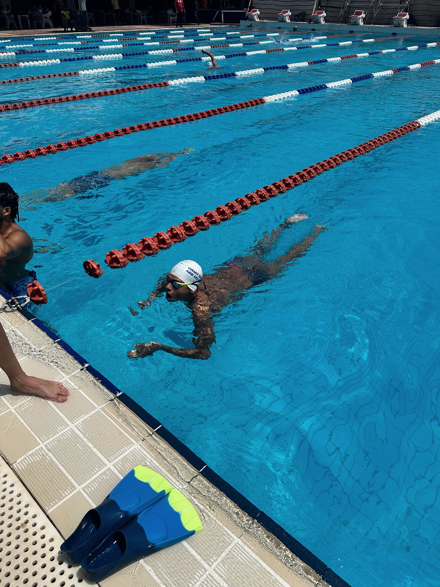 A swimmer working along the lane rope, fins waiting on the deck