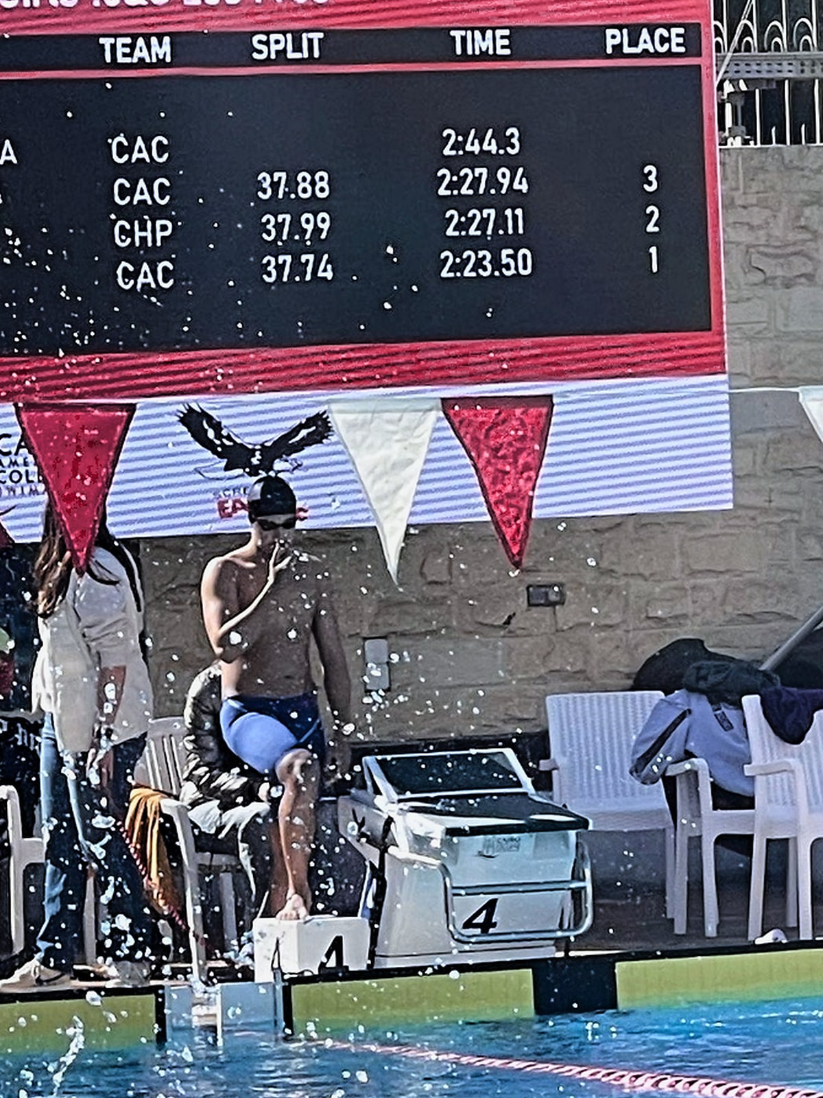 A swimmer diving off the blocks beneath a results board showing splits, times and places