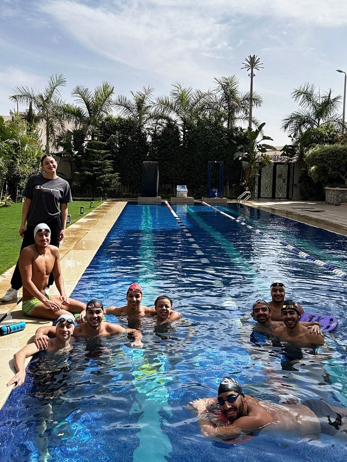 SWEEP swimmers in the water at the side of the pool, with the deck and trees behind them
